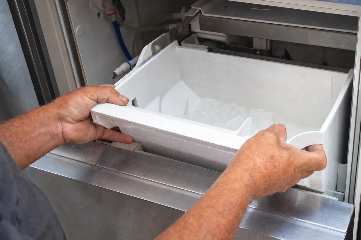 An undercounter ice machine built into a run of cabinets, its bin pulled forward for inspection