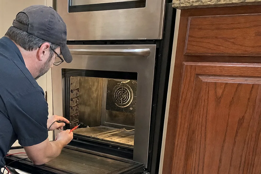 The lower corner of an open oven door with a screwdriver and a torch lying on the protective cloth